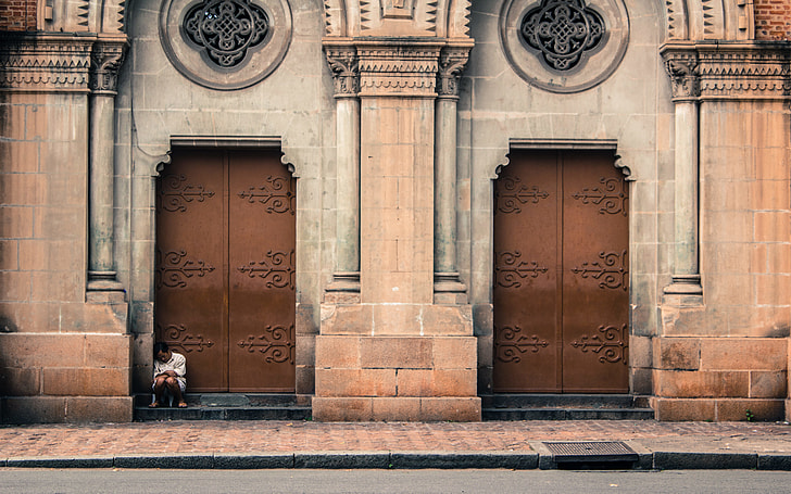 photo of person sitting beside cathedral door