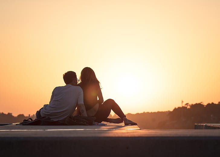 photo of man and woman sitting on sea shore during sunset