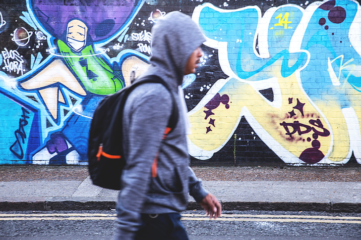 A man with a hooded-top and rucksack walks past the graffiti-covered streets of Shoreditch in East London