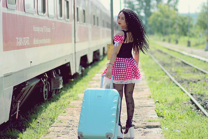 woman wearing red, white, and black polka-dot dress pulling teal luggage