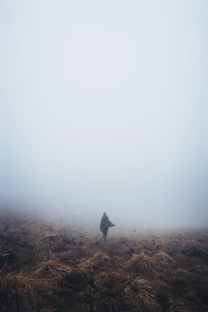 person wearing cape standing on brown ground soil under fog