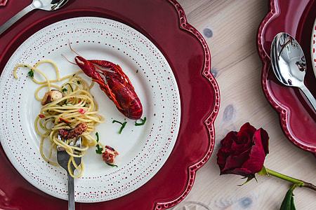 Fancy dinner with seafood pasta, crayfish and red wine by the table decorated with roses