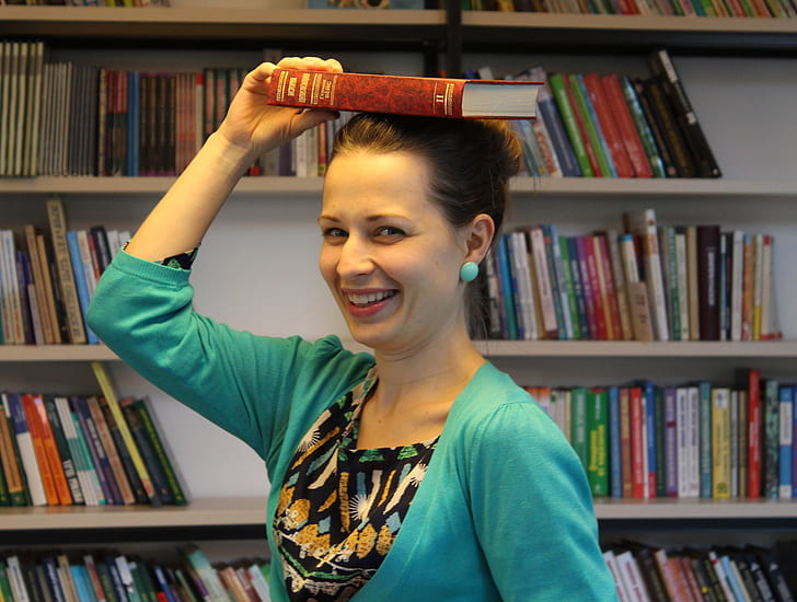 woman placing book on top of her head while smiling