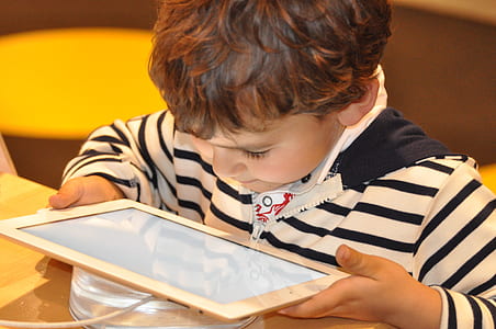 boy in white and black striped shirt holding white tablet computer