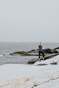 woman wearing gray tank top and black leggings standing on boulder near body of water