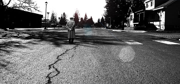 grayscale photography of man wearing overcoat standing on road