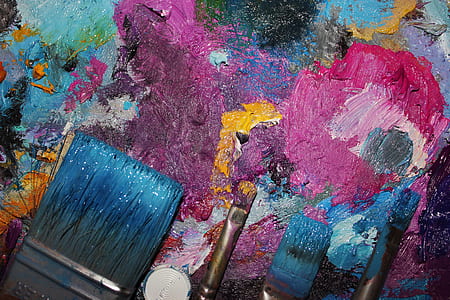 four paintbrushes on top of pink, blue, and pink abstract painting