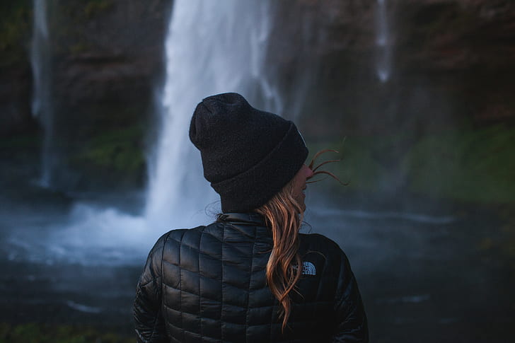 woman in black knit cap standing in front waterfalls