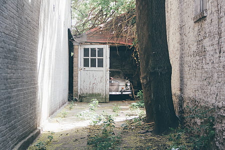 vintage white car inside of opened garage by the alley