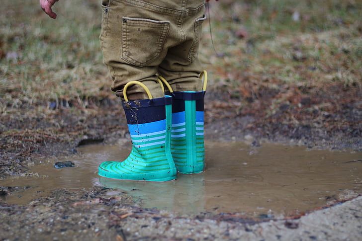 person with brown denim pants tea-and-black rain boots on body of water during daytime