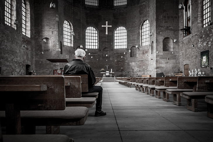 man in black jacket on wooden chair inside church