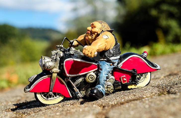 selective focus photo of man in white shirt ride on red and black cruiser motorcycle scale model