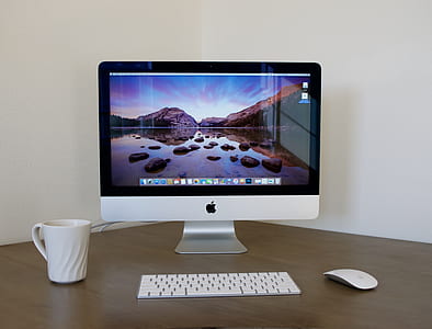 silver iMac, magic keyboard, and magic mouse on top of brown wooden table