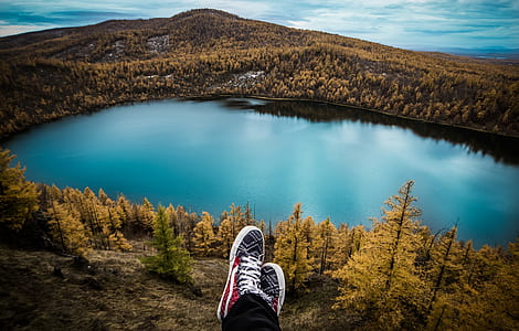 person wearing red-and-white sneakers sitting in front lake