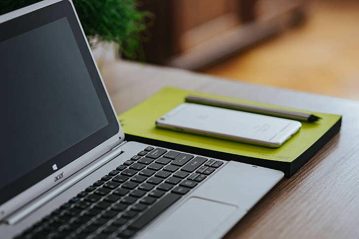 Silver Acer laptop, a white Apple iPhone and a notepad on a wooden desk