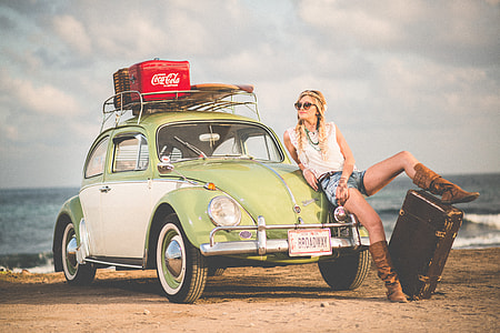 woman seats on green Volkswagen Beetle parked at seashore during daytime