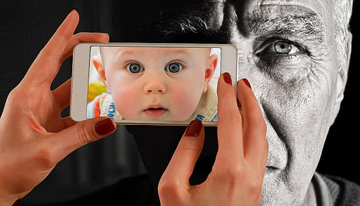person holding white smartphone with baby's face wallpaper