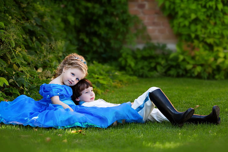 two girl and boy wearing dresses lying down on green grass field