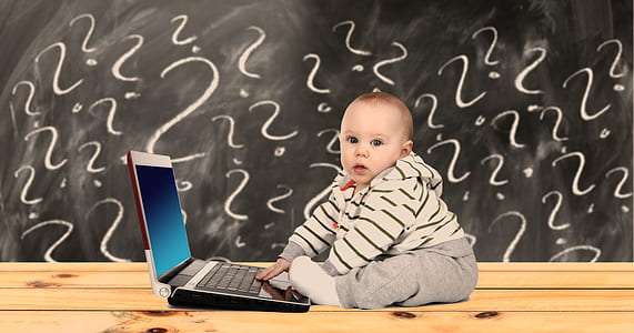 toddler boy wearing hoodie and grey pants sitting beside grey laptop computer