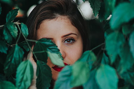 black haired woman hiding behind green leaves