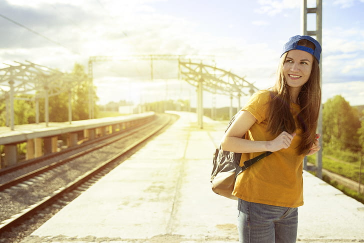 woman wearing yellow crew-neck t-shirt, blue cap, and carrying backpack