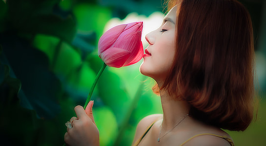 woman smelling pink lotus flower bud at daytime