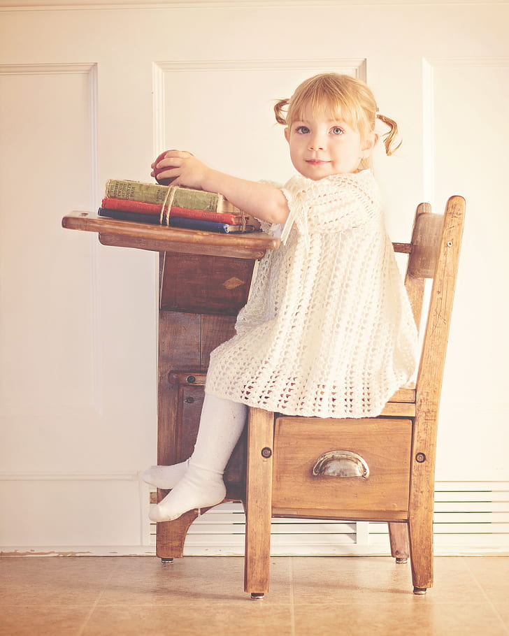 girl in white knitted dress sitting on brown wooden school chair