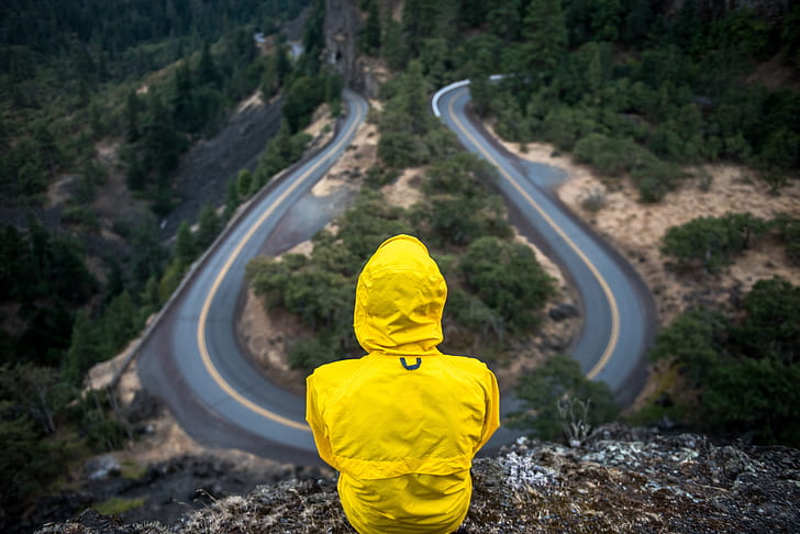 person wearing yellow coat sitting on mountain edge