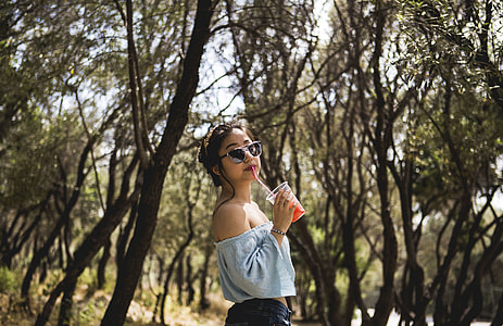woman holding plastic cup sipping under trees