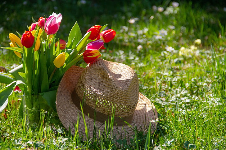 brown straw hat on grasses near tulip flowers