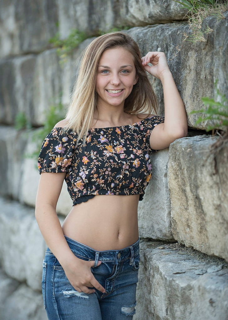 woman in black and yellow floral crop top and blue jeans leaning on wall