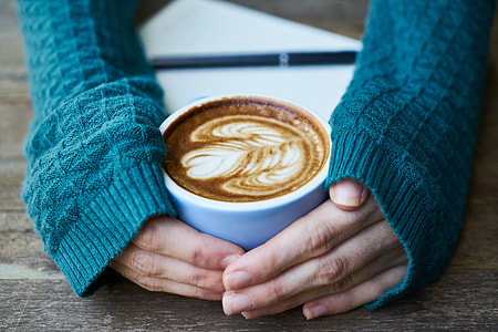woman wearing blue knitted long-sleeved shirt holding white ceramic teacup