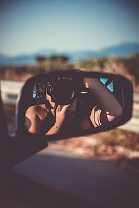 selective focus photography of car side mirror reflected the woman taking the picture using DSLR camera while inside the car