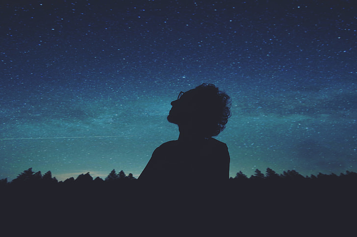 silhouette of person wearing glasses looking at the sky during nighttime