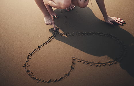 close-up photo of woman drawing heart on sand