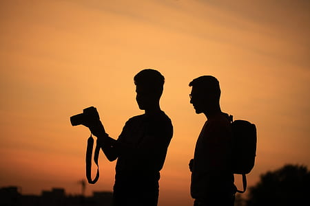 silhouette of two men carrying camera and backpack during sunset