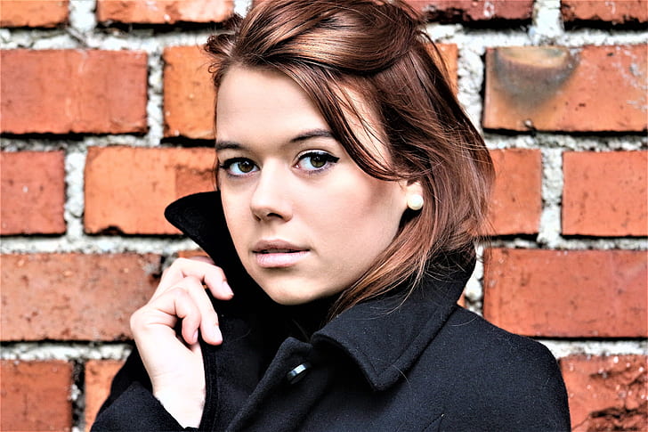 closeup photo of woman wearing black coat near brick wall