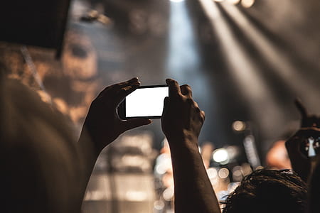 selective focus photography of person holds smartphone in portrait mode during concert