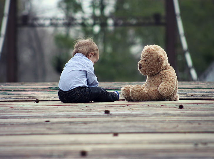 boy sitting next to brown bear plush toy during daytime