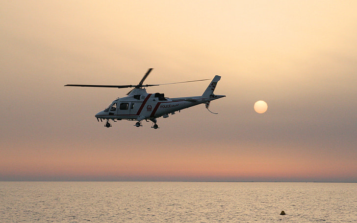 white helicopter hovering above body of water