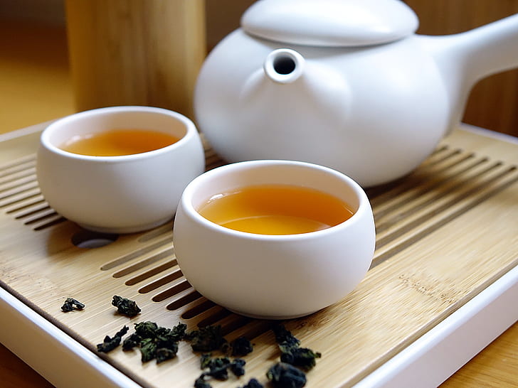 white ceramic teacup with tea near teapot on table