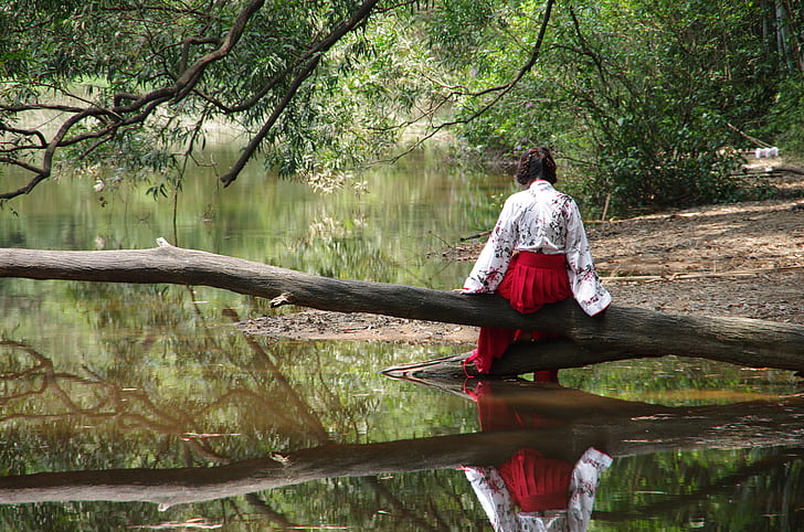 woman wearing red bottoms sitting on tree branch on body of water