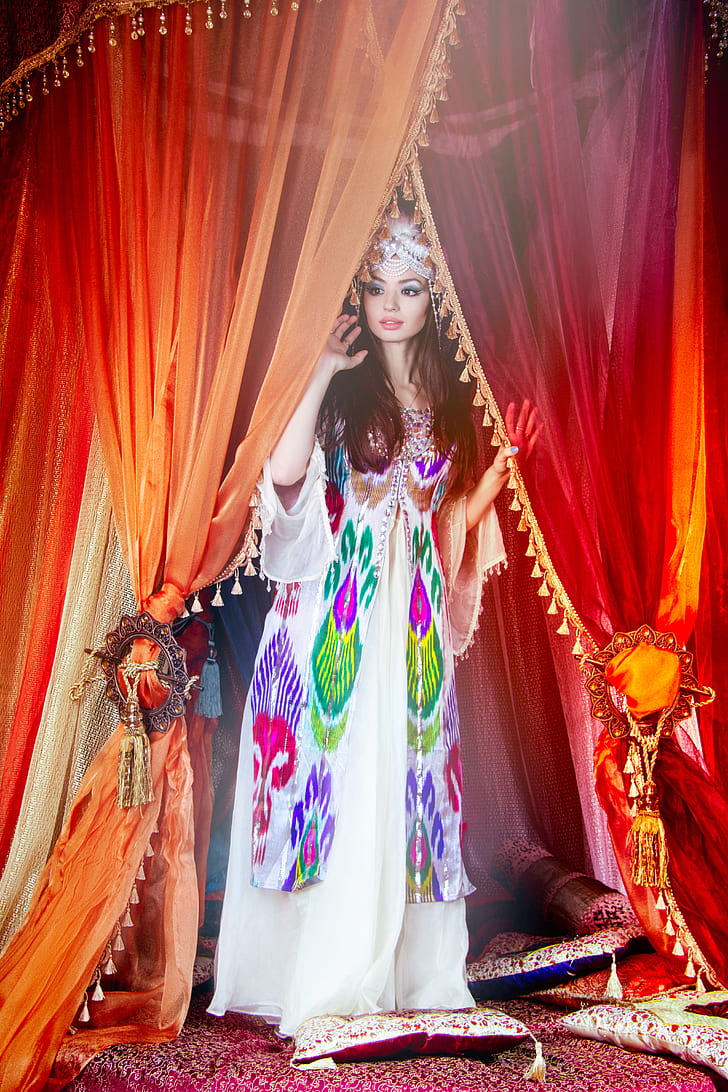 woman standing while holding orange and red curtain wearing multicolored angel sleeve long dress