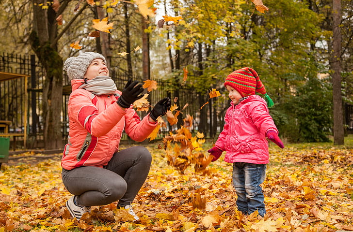 woman in red sweater tossing upward some brown leaves while a girl playing with it
