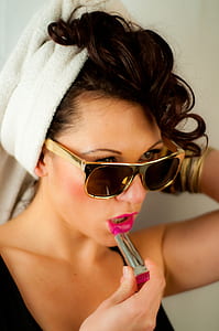 woman wearing gold sunglasses while applying lipstick