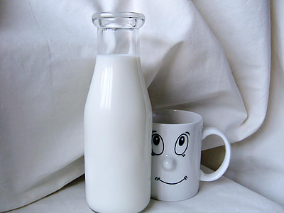 person taking photo of milk glass bottle beside white ceramic mug