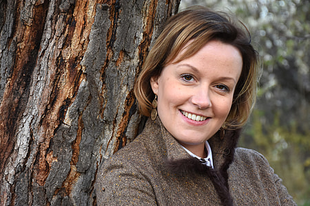 woman wearing brown collared jacket leaning on tree trunk