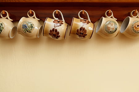 six assorted-color floral ceramic teacups hanged on brown wooden wall-mounted shelf with hooks