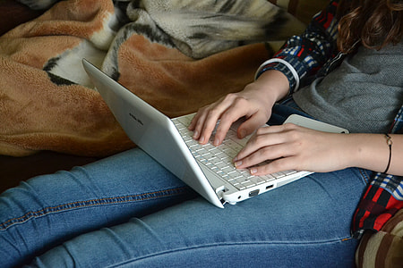woman wearing gray long-sleeved shirt and blue jeans with white laptop on lap