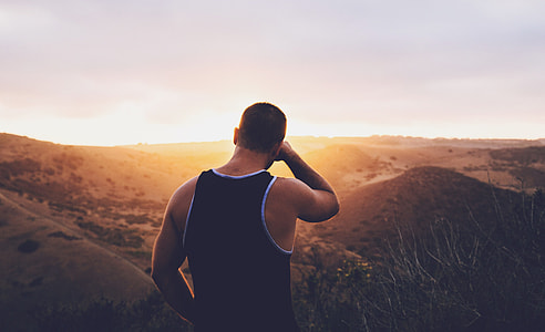 man in black tank top standing on hill during golden hour